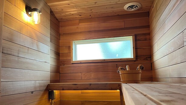 Un sauna en bois, avec un banc, une fenêtre et un seau en bois.