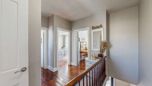 Un couloir avec un plancher en bois, un escalier avec une rampe en bois et une porte donnant sur une chambre à coucher.