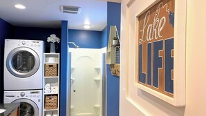 Une buanderie équipée d’un lave-linge, d’un sèche-linge et d’un espace douche fermé par des parois en verre.