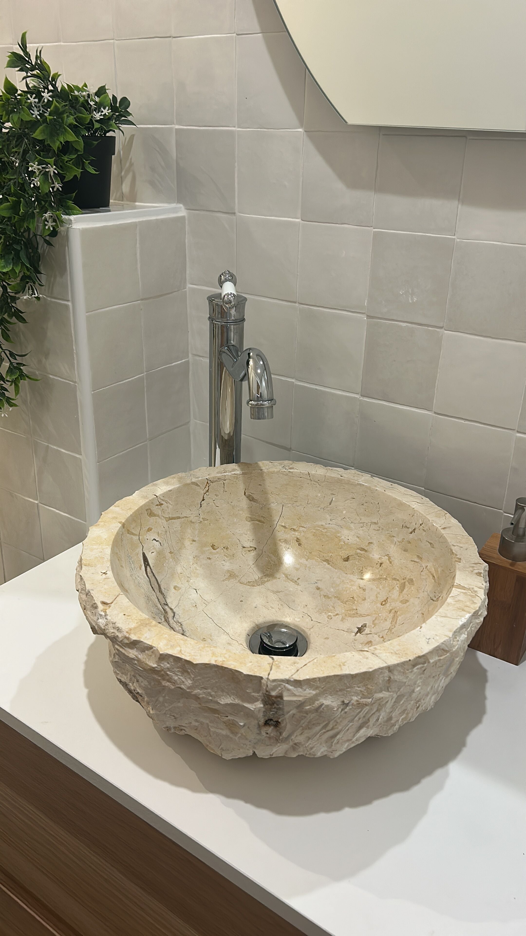 Un lavamanos de piedra con un grifo moderno en un baño con azulejos blancos y una planta en maceta.