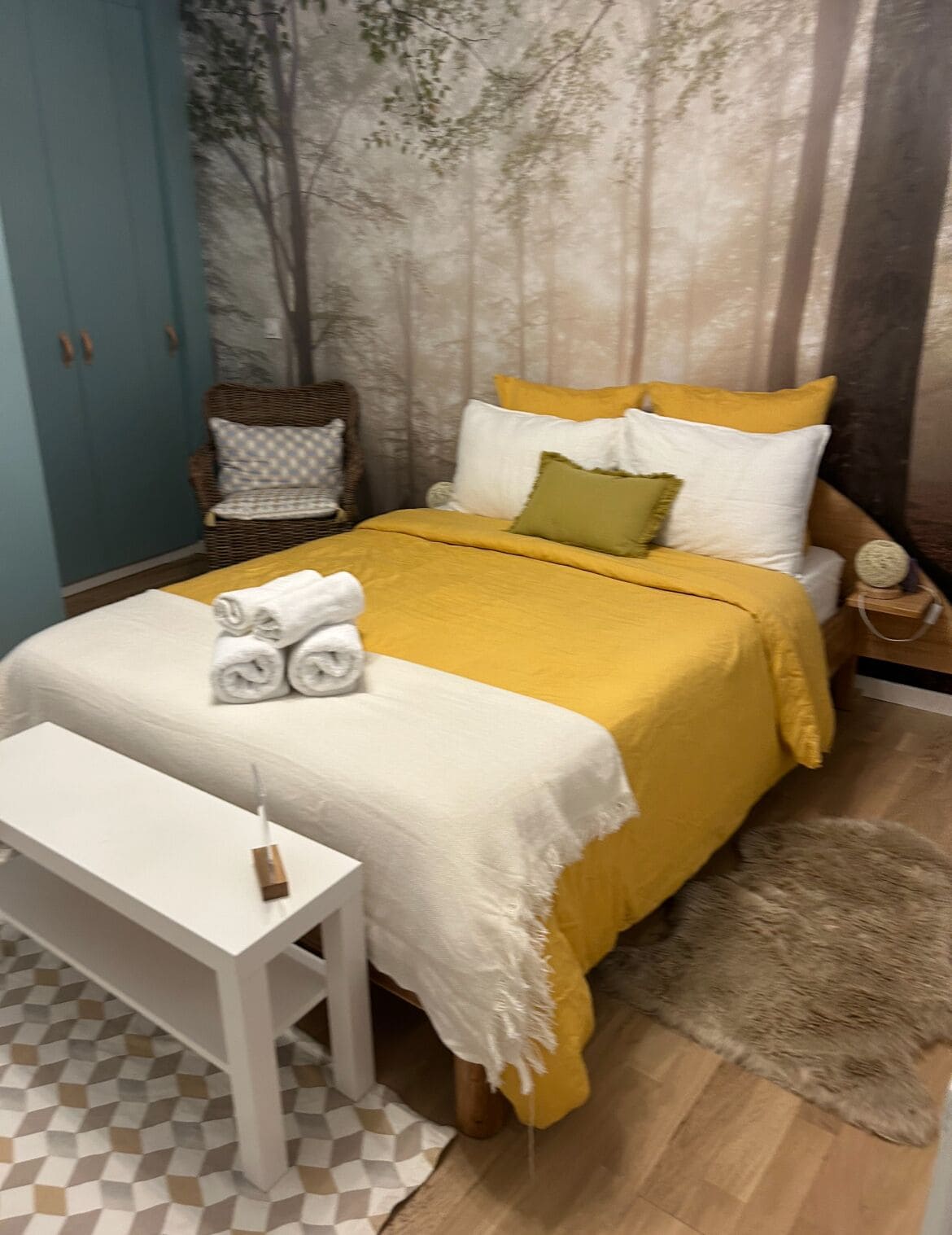 A bedroom with a bed, a bench, a chair, and a wall mural.
