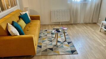 Een woonkamer met een gele bank, een vloerkleed met patroon en een kleine bijzettafel.