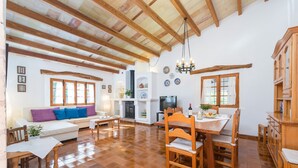 Un vaste espace de vie doté d’un plafond en bois, d’une table à manger avec des chaises, d’un canapé avec des coussins et d’un téléviseur.