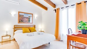 Ein Schlafzimmer mit einem großen Bett, einem Holzkopfende, Nachttischlampen, einem gerahmten Bild an der Wand, einem Nachttisch aus Holz, einem Tisch mit einem Stuhl und einer Topfpflanze.