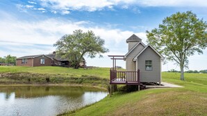 A residential area with a pond, a small cabin with a deck, and a larger house in the background. - Angela’s Ashlake Farm Estate Hancock Co. (Poplarville)
