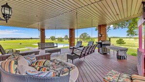 A covered outdoor deck with wicker furniture, a grill, and a view of a green field. - Angela’s Ashlake Farm Estate Hancock Co. (Poplarville)