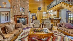 A spacious living room with a fireplace, comfortable seating, and a kitchen area in the background. - Angela’s Ashlake Farm Estate Hancock Co. (Poplarville)