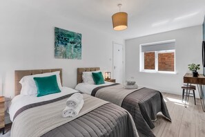 Une chambre d’hôtel moderne avec deux lits, une grande fenêtre donnant sur un mur de briques, un tableau au mur et un bureau agrémenté d’une plante.