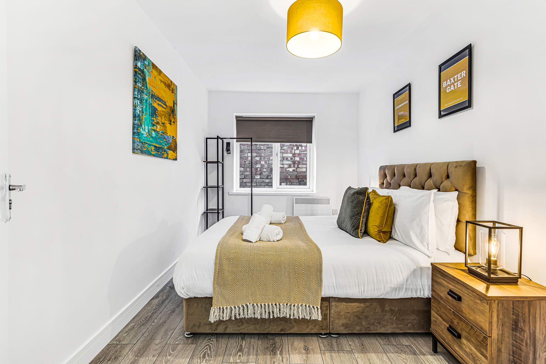 A bedroom with a bed, bedside table, lamp, and artwork on the wall.