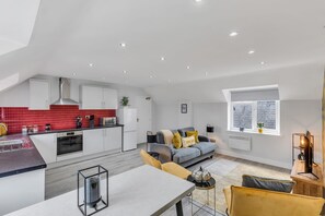 Een moderne keuken met rode tegels, een eethoek met een tafel en stoelen, en een woonkamer met een bank en een raam.