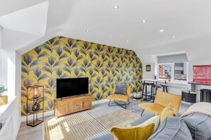 A modern living room with a large flat-screen TV, a wooden entertainment unit, and a yellow patterned wall.