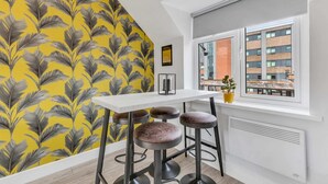 A modern kitchen with a white countertop, three stools, and a yellow leaf-patterned wall.