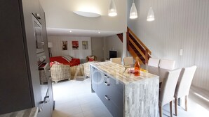 Eine moderne Küche mit einer Marmorinsel, eine Essecke mit einem roten Sofa und eine Treppe, die zu einer weiteren Ebene führt.