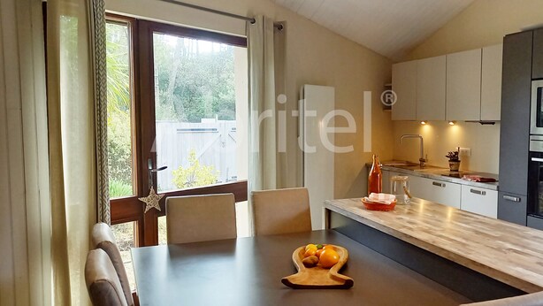 Eine moderne Küche mit Einbauofen, ein Essbereich mit Holztisch und Stühlen sowie ein Blick ins Freie durch ein großes Fenster.