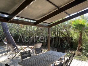 Relax in a shaded patio surrounded by lush greenery, complete with a table and chairs.