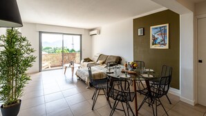 A modern living room with a dining area, a large potted plant, a sofa, and a table set for dining. - Apartment 4P 97M2 Sea view city center (Porto-Vecchio)