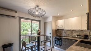 A modern kitchen with a dining area, featuring a large window, a hanging light fixture, and a trash bin. - Apartment 4P 97M2 Sea view city center (Porto-Vecchio)