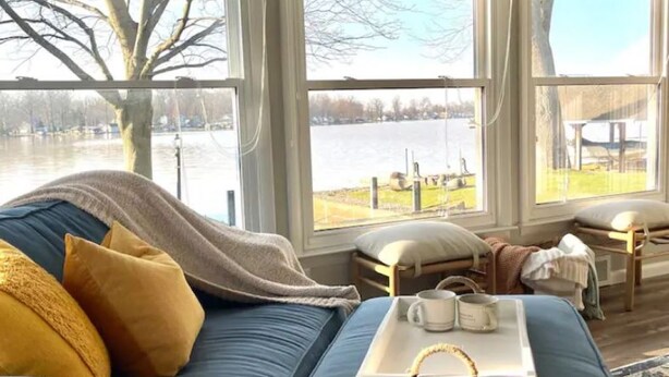 A cozy living room with a blue sofa, a coffee table with a tray, and large windows overlooking a body of water. - Lakefront views at our Long Island Lookout! (Belle Center)