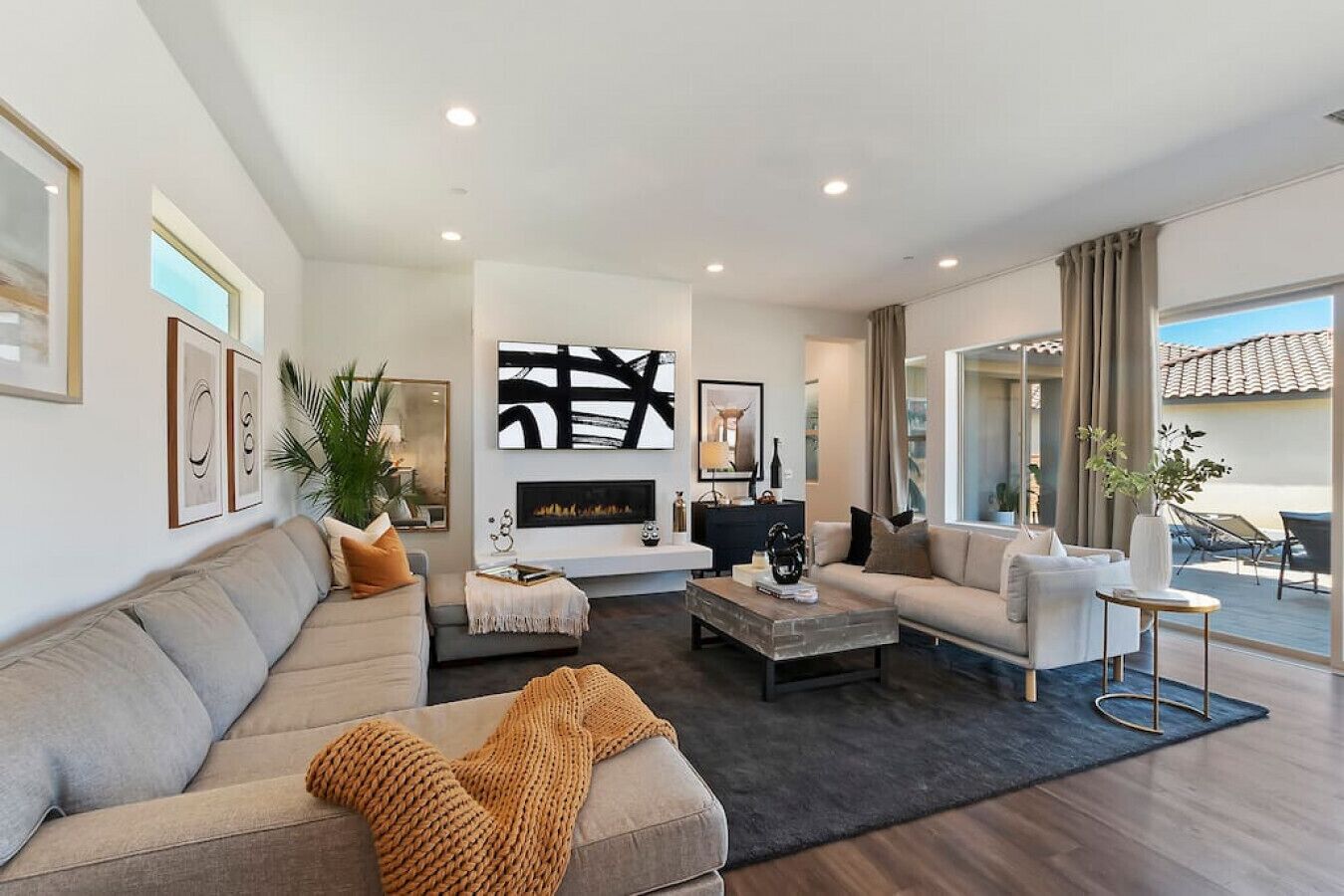 A modern living room with a fireplace, a sofa, a coffee table, and a dining area with outdoor seating.