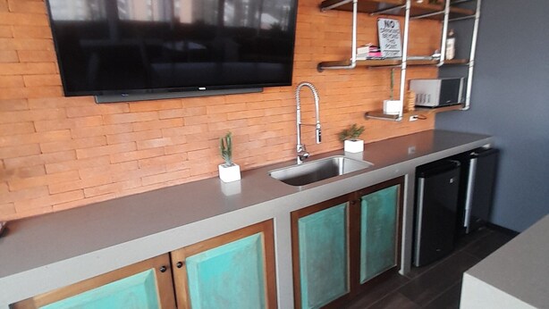 A modern kitchen with a flat-screen TV, stainless steel sink, and wooden cabinets.