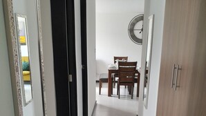 A hallway with a dining area at the end, featuring a wooden table and chairs.