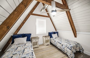 A bedroom with two beds, wooden beams, a sloped ceiling, a window with blinds, and a ceiling fan. - Minutes from the Beach!<br>A-Frame at The Point (Pensacola)