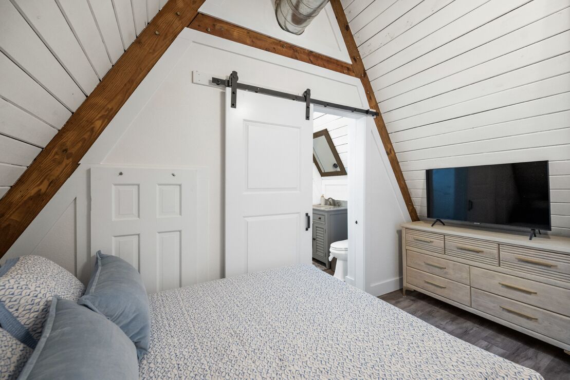 A bedroom with a sloped ceiling, a bed with patterned bedding, a dresser, and a television.