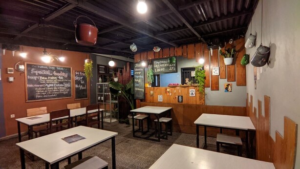 Un café acogedor con mesas y sillas de madera, un menú en la pizarra y una decoración rústica.
