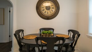 Een eethoek met een ronde tafel, vier stoelen, een klok aan de muur en een kleine plant op de tafel.
