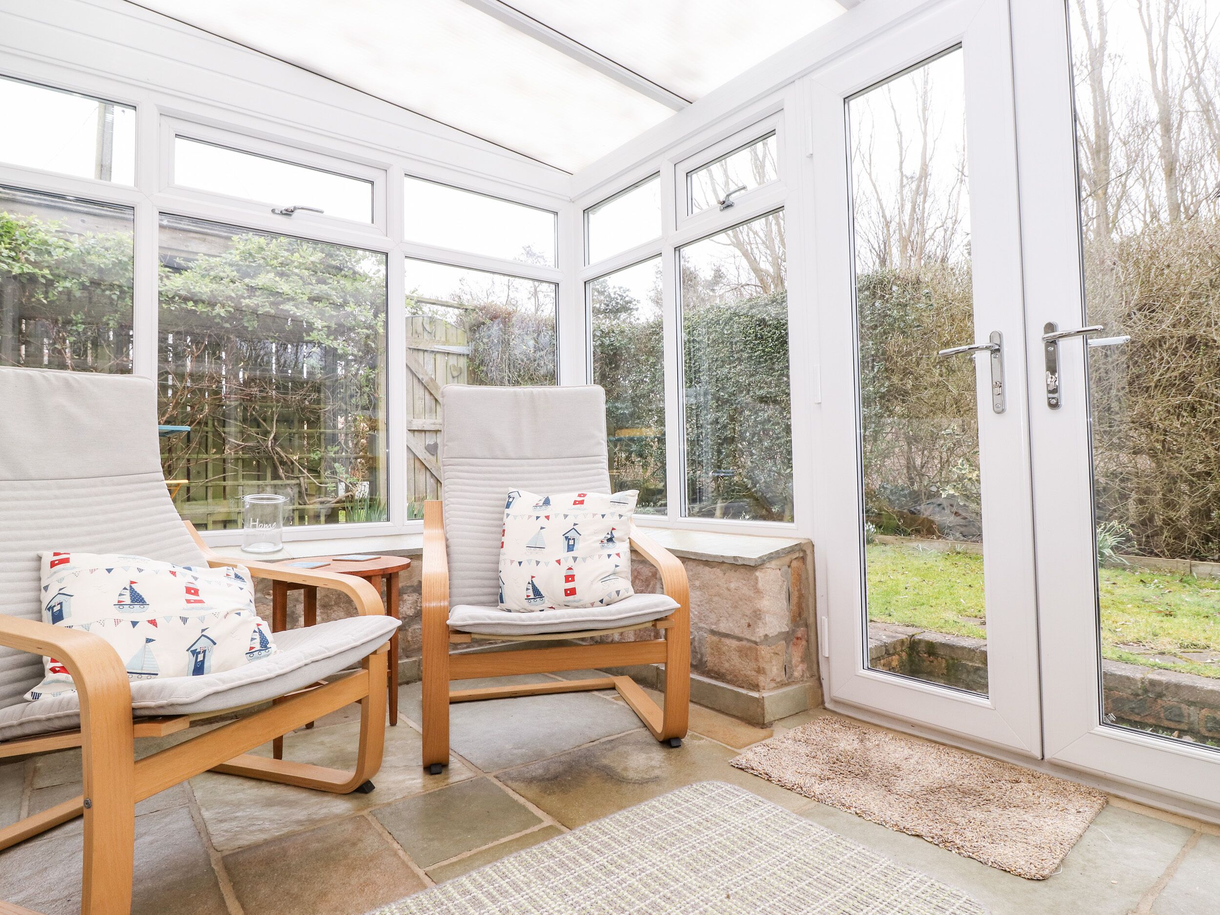 A conservatory with two wooden chairs, a small table, and a glass door leading outside.