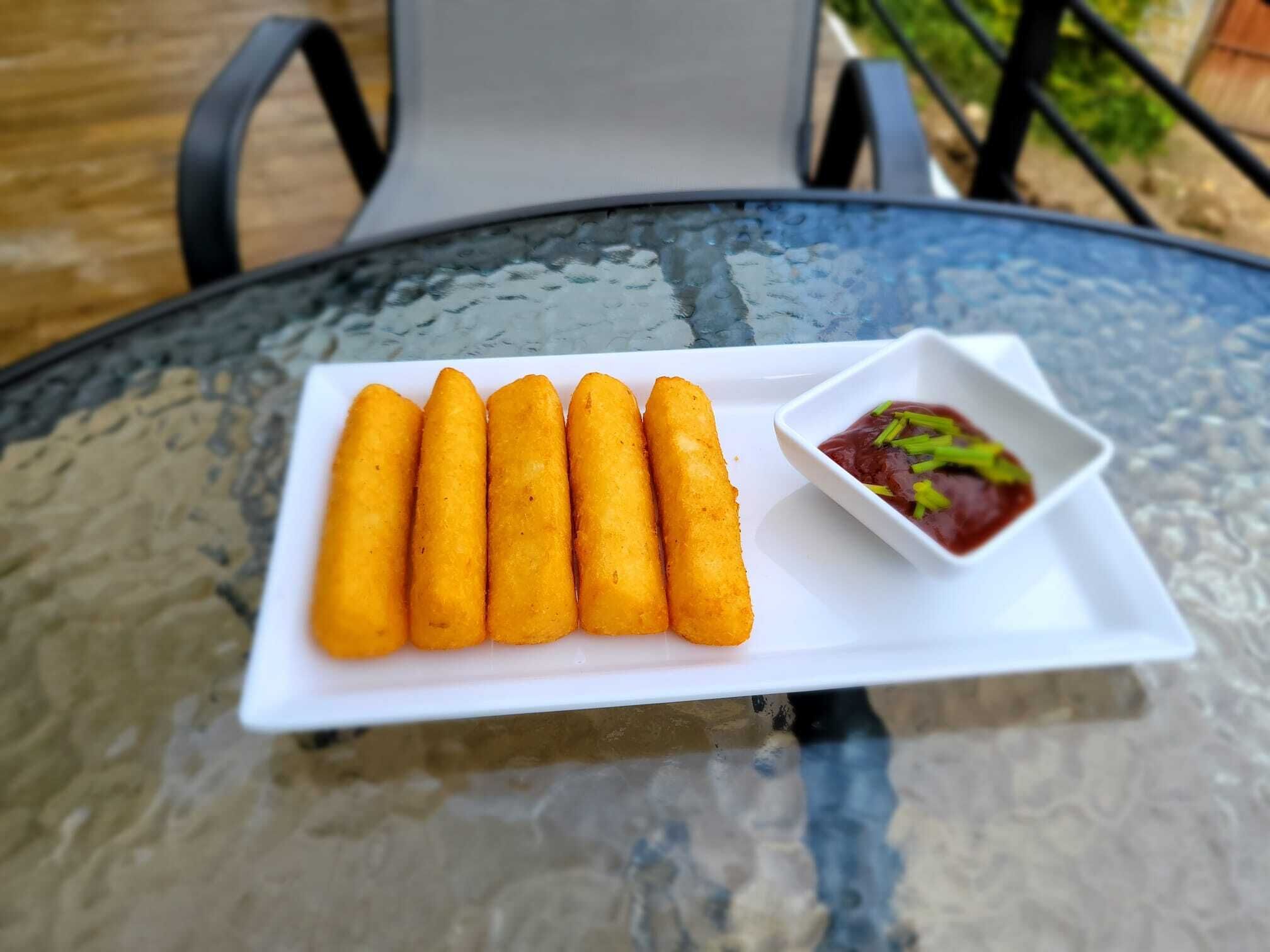 Una mesa de cristal con un plato blanco de croquetas doradas y un cuenco pequeño de salsa roja para mojar.