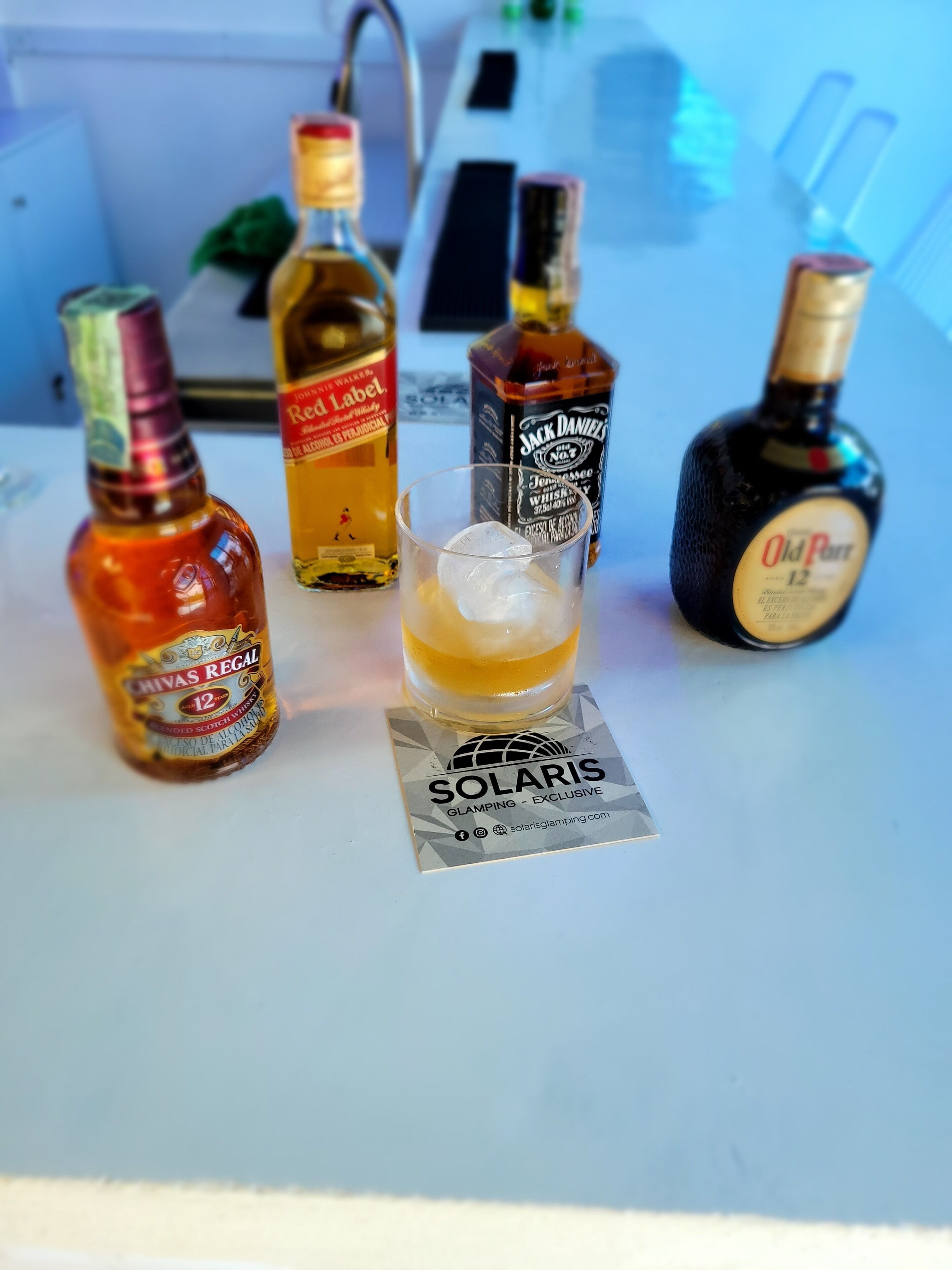 Un bar avec différentes bouteilles de whisky et un verre de whisky servi avec des glaçons.