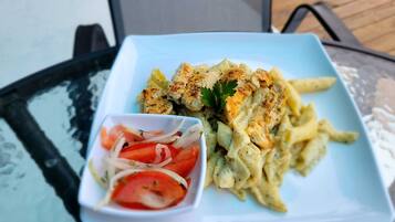 A plate of pasta with chicken and a small bowl of tomato salad on a glass table.