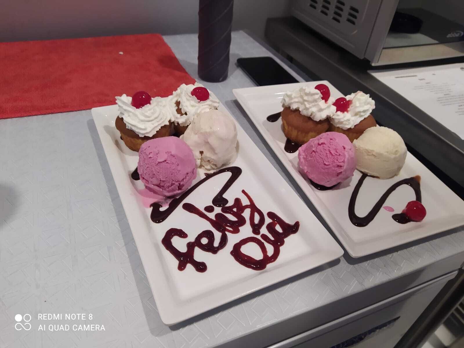 Dos platos de postre con helado y crema batida, uno con un adorno rojo que dice 'Feliz Dia'.