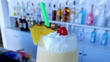 Cóctel con una rodaja de piña y una cereza en un vaso, frente a una barra con varias botellas al fondo.