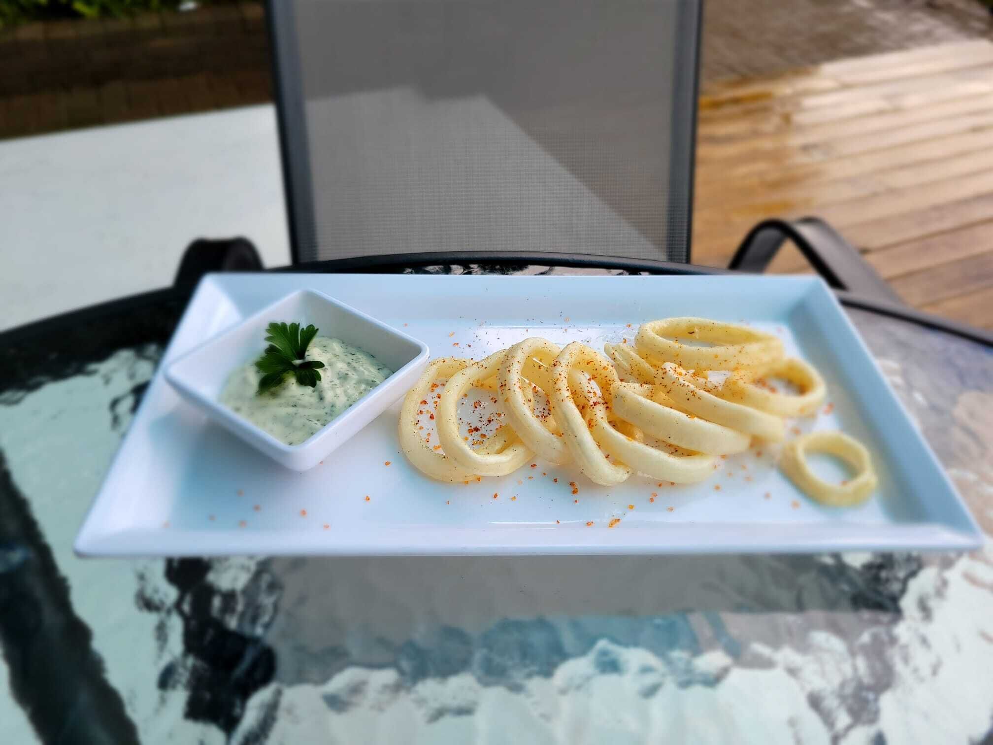 A plate of pasta with a side of sauce and a small bowl of garnish on a table.