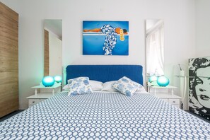 Un dormitorio con una colcha estampada, un cabecero azul, dos lámparas de noche y un cuadro en la pared.