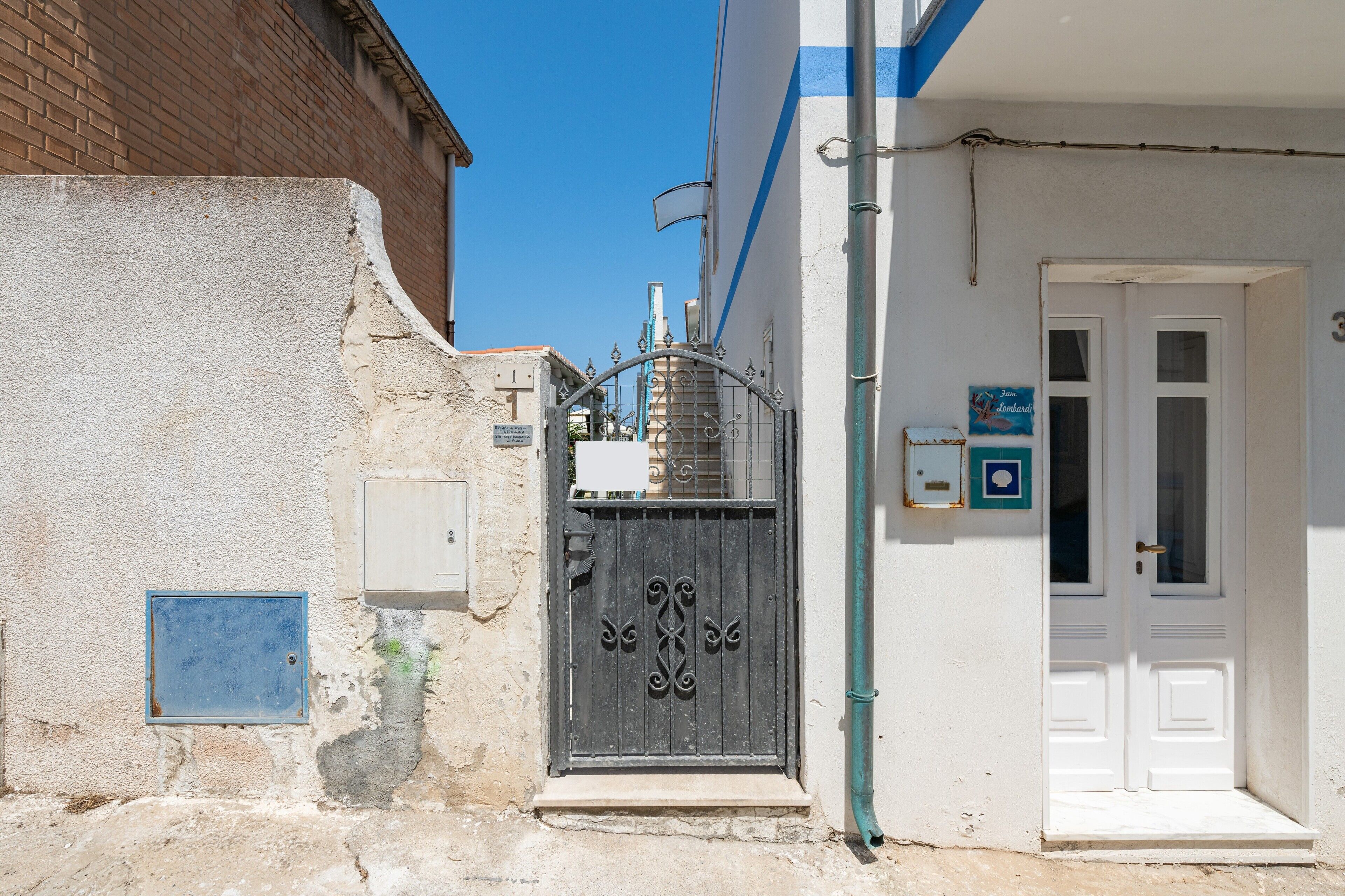 A narrow street with a white building, a metal gate, and a blue sign.