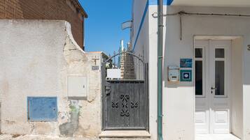 A narrow street with a white building, a metal gate, and a blue sign.