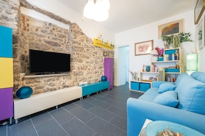 Una sala de estar con una pared de piedra, un televisor de pantalla plana, un sofá azul y una estantería.