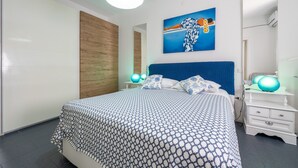 A bedroom with a bed, a nightstand, a dresser, a wall-mounted painting, and a ceiling light fixture. - Apartment 'Casa Nora' with Private Terrace, Wi-Fi and Air Conditioning (Calasetta)