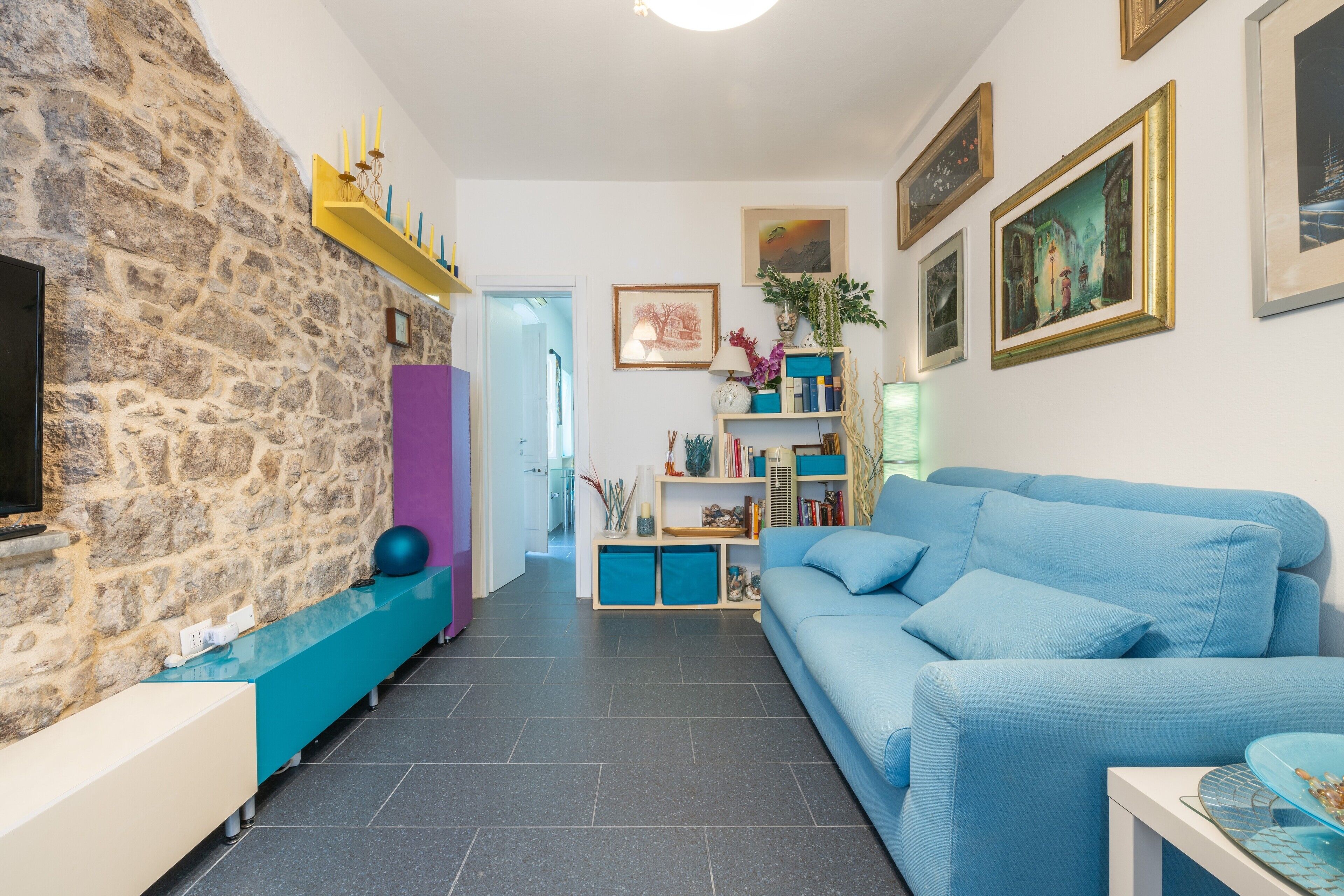 Ein Wohnzimmer mit einer Steinsäule, einem blauen Sofa, einem Fernseher und einem Bücherregal.