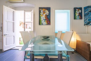 Un comedor con mesa de vidrio, cuatro sillas, un sofá de mimbre y dos cuadros colgados en la pared.