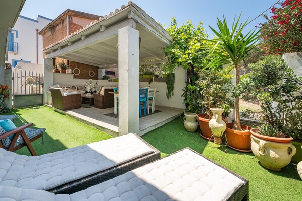 Un área de estar al aire libre techada con patio, césped artificial y plantas en macetas.