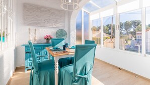 A dining area with teal chairs, a wooden table, and a large window with a view of buildings. - Holiday Home "El Pinito Moraira" with Private Terraces, Private Pool & Wi-Fi (Moraira)