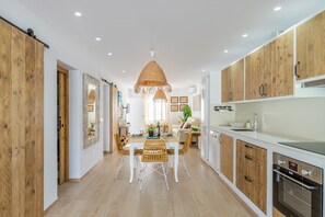 A modern kitchen with wooden cabinets, a dining area with wicker chairs, and a large pendant light.