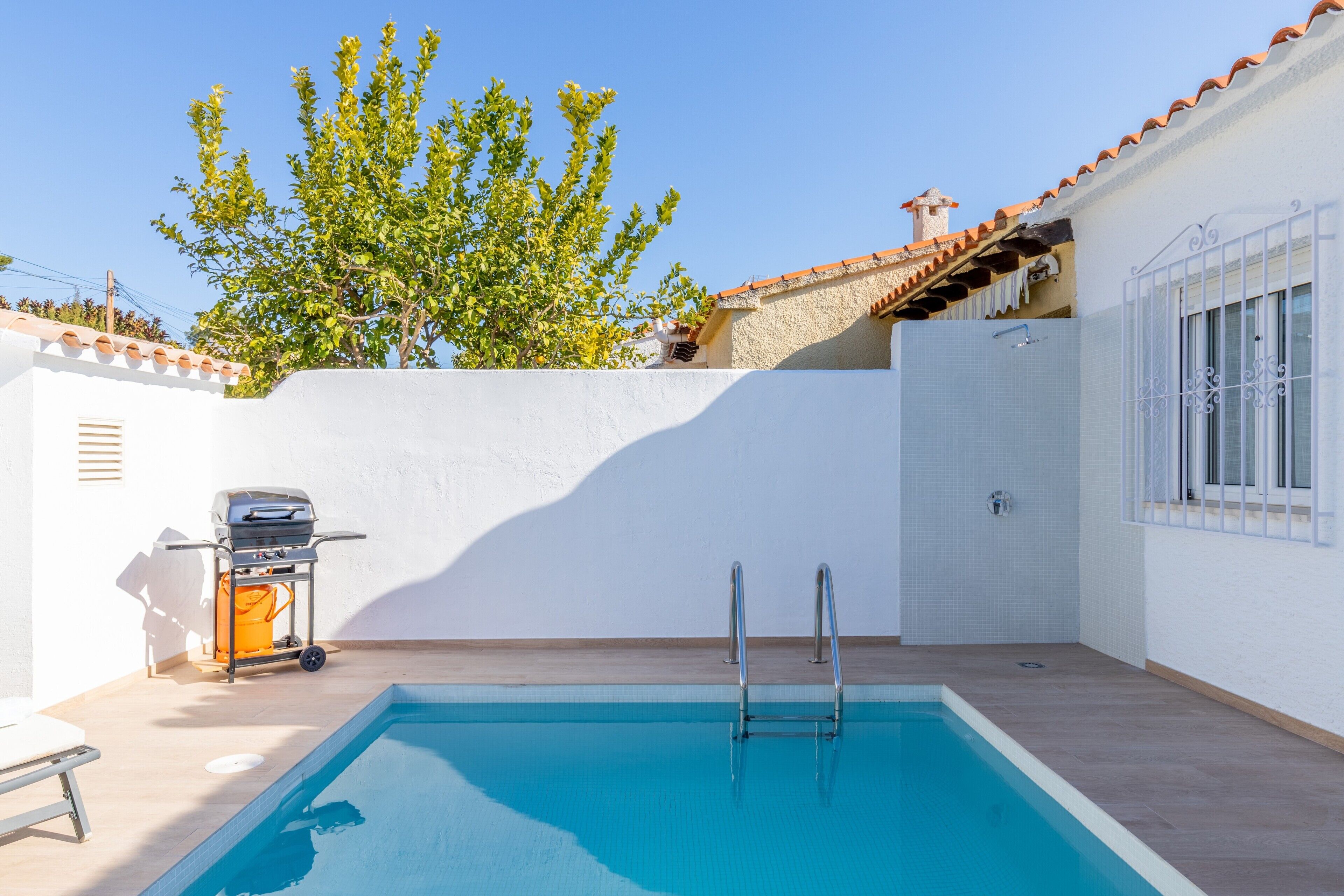 Une piscine avec un escalier, un barbecue et un arbre en arrière-plan.