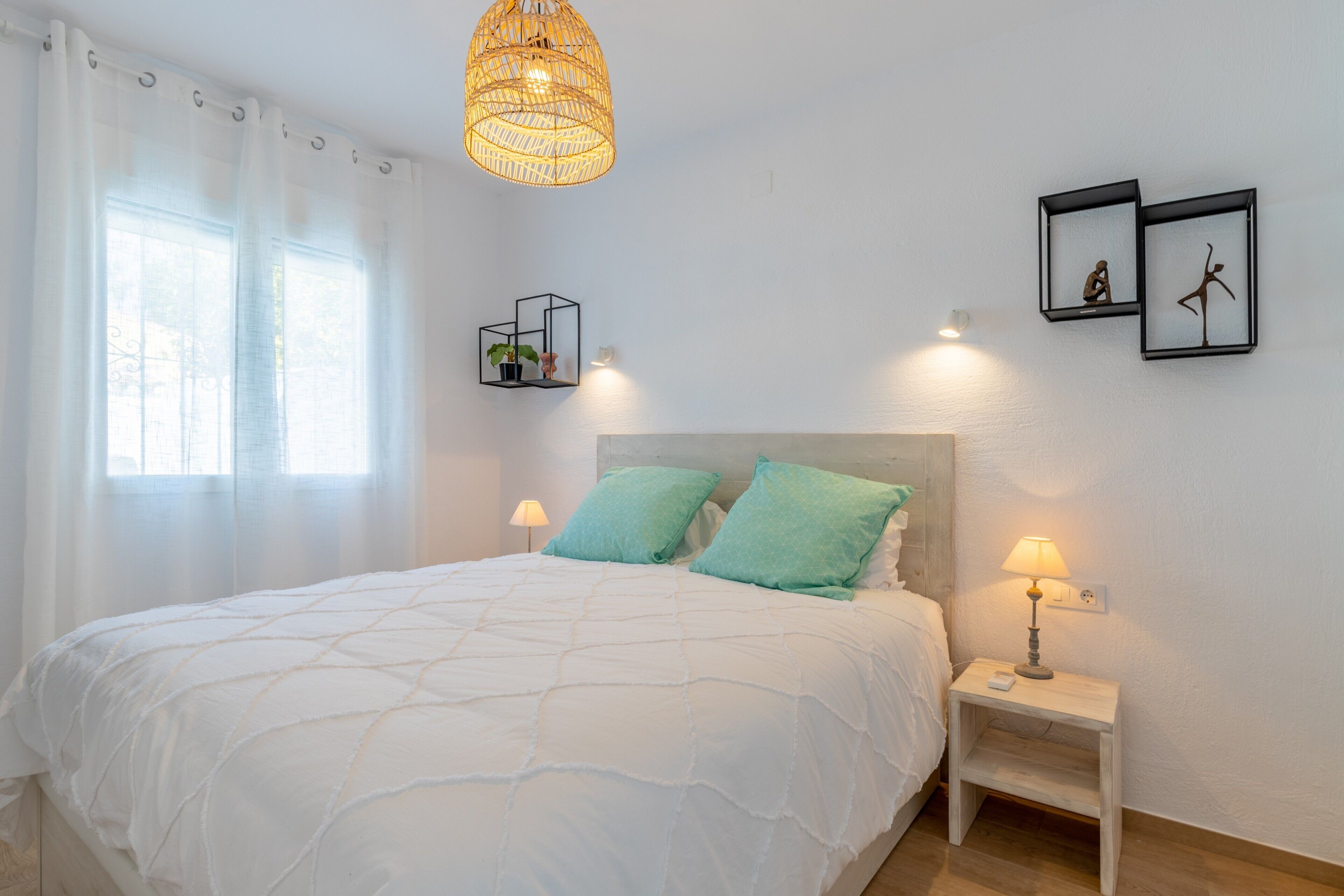 A bedroom with a bed, bedside table, lamp, wall-mounted shelf, and two framed pictures.