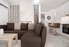 En moderne stue med en hjørnesofa, et spisebord og et køkken med komfur.