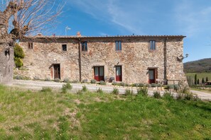 A stone building with multiple windows and doors, a gravel driveway, and a grassy foreground. - Apartment 'Rifugio sulla via di Volpaia' with Private Terrace, Wi-Fi and Air Conditioning (Radda in Chianti)